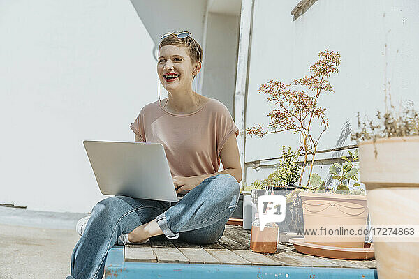 Frau lachend bei der Benutzung eines Laptops auf der Terrasse an einem sonnigen Tag
