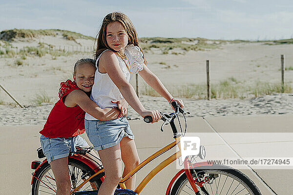 Jüngere Schwester umarmt Mädchen auf dem Fahrrad sitzend an einem sonnigen Tag