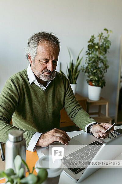 Älterer Mann  der eine Kreditkarte benutzt  während er zu Hause am Laptop arbeitet