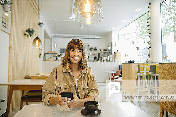 Geschäftsfrau  die in einem Café sitzt und ihr Smartphone benutzt