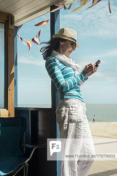 Woman using smart phone while standing in beach hut on sunny day