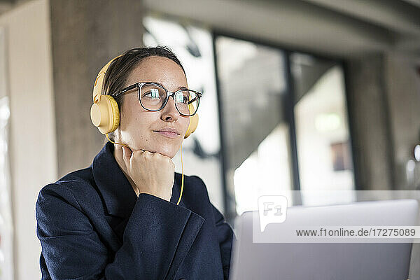 Businesswoman with head in hands and headphones using laptop while sitting at office