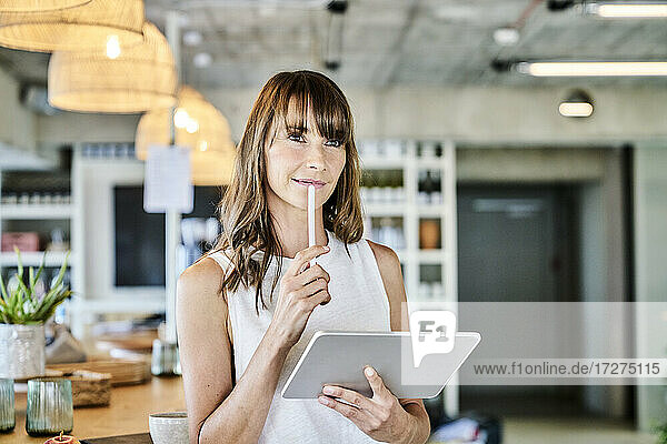 Nachdenkliche Frau  die einen digitalen Stift und ein digitales Tablet hält  während sie zu Hause steht