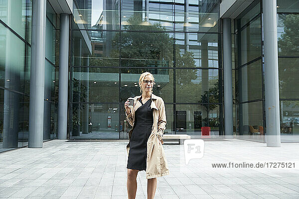 Lächelnde Frau mit Kaffeetasse vor einem Bürogebäude