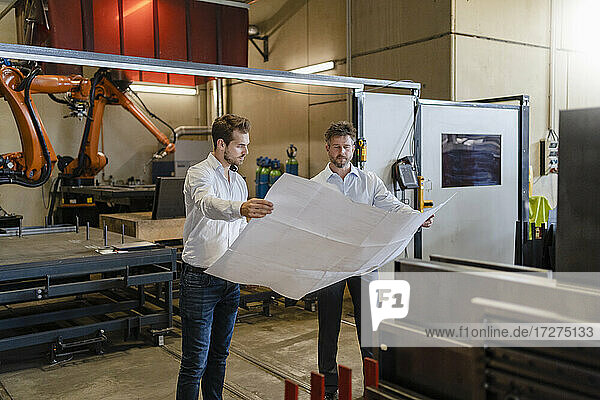 Geschäftsleute studieren den Bauplan eines Unternehmens  während sie vor einer automatisierten Maschine in einer Fabrik stehen