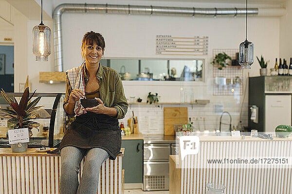 Lächelnde Besitzerin mit Kaffeetasse auf dem Tresen eines Cafés