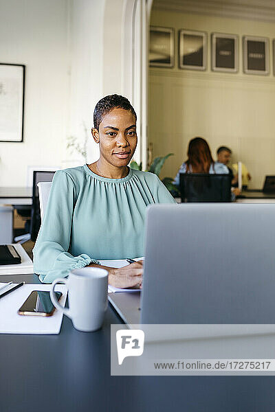 Lächelnde Geschäftsfrau bei der Arbeit am Laptop im Büro