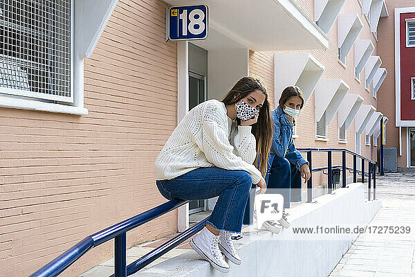 Betrachtung von Freundinnen mit Gesichtsmaske auf dem Geländer sitzend bei covid-19