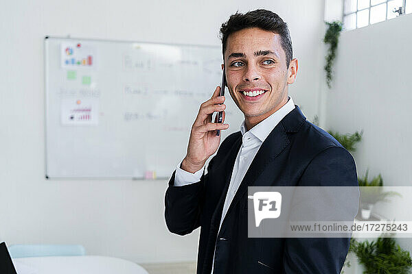 Happy male professional looking away while talking on phone at workplace