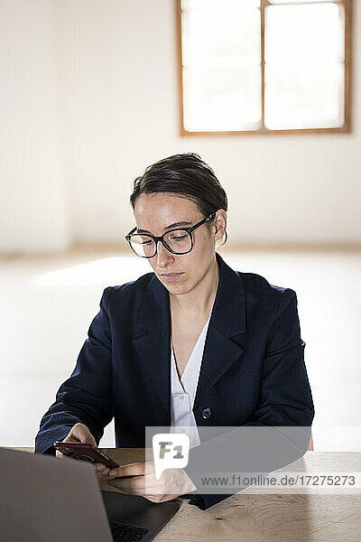 Businesswoman using mobile phone while sitting by table at office