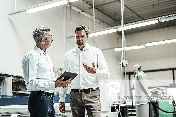 Mature businessman discussing with colleague over digital tablet in industry