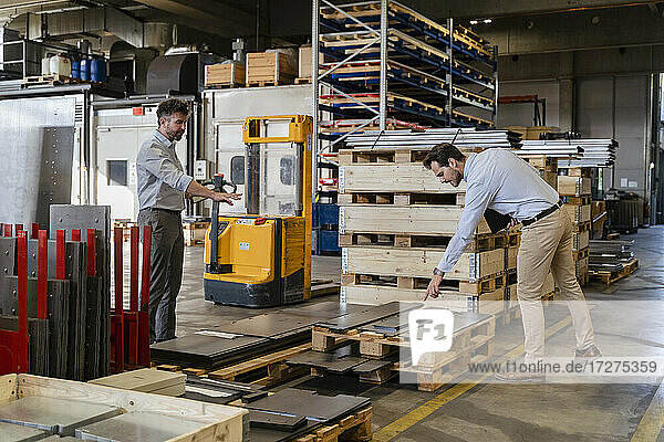 Geschäftsleute inspizieren Metallmaterial  während sie in einem Lagerhaus in einer Fabrik stehen