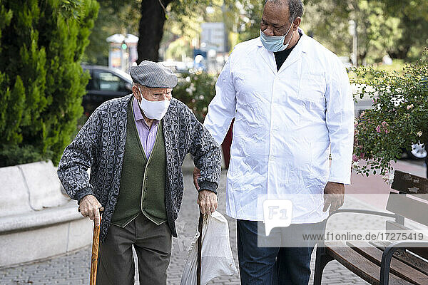Reifer Mann mit älterem Mann mit Gesichtsschutzmaske beim Spaziergang im Freien