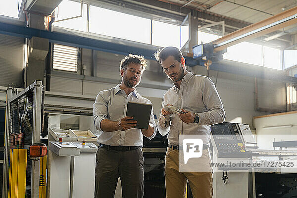Geschäftsleute benutzen ein digitales Tablet  während sie in einer Fabrik ein Metallobjekt untersuchen