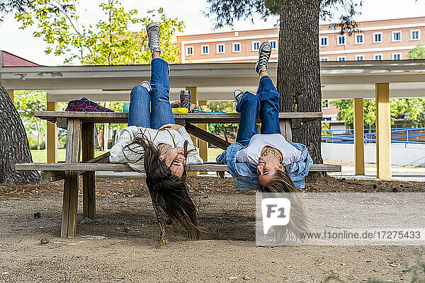 Weibliche Freunde liegen auf einer Bank kopfüber in einem öffentlichen Park an einem sonnigen Tag