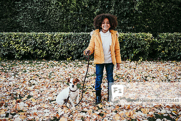 Lächelndes Mädchen hält Haustier Leine  während stehend von Hund im Park