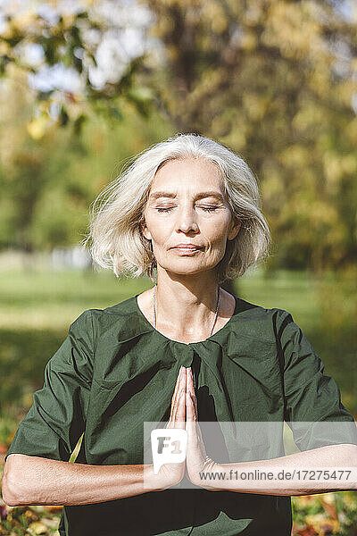 Frau sitzt mit verschränkten Händen im Park und macht Yoga