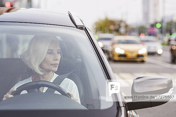 Reife Geschäftsfrau schaut in den Seitenspiegel beim Autofahren in der Stadt