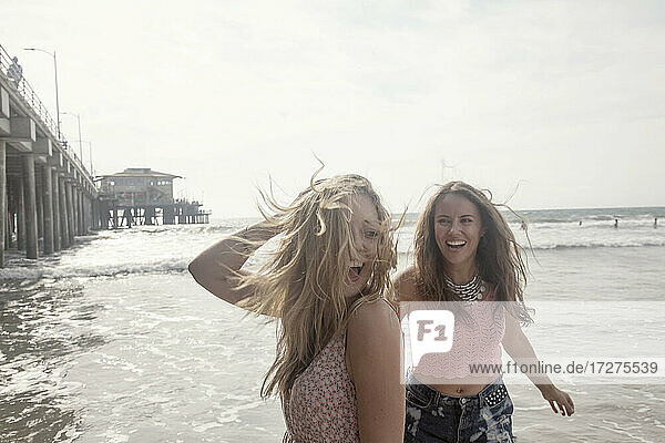 Young female friends enjoying weekend at beach against clear sky