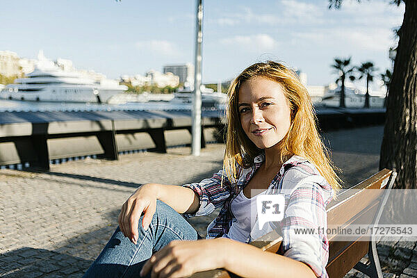 Junge Frau sitzt auf einer Bank an einem sonnigen Tag