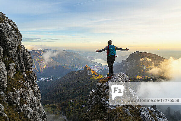 Nachdenklicher Wanderer mit ausgestreckten Armen auf einem Berg stehend während des Sonnenaufgangs in den Bergamasker Alpen  Italien
