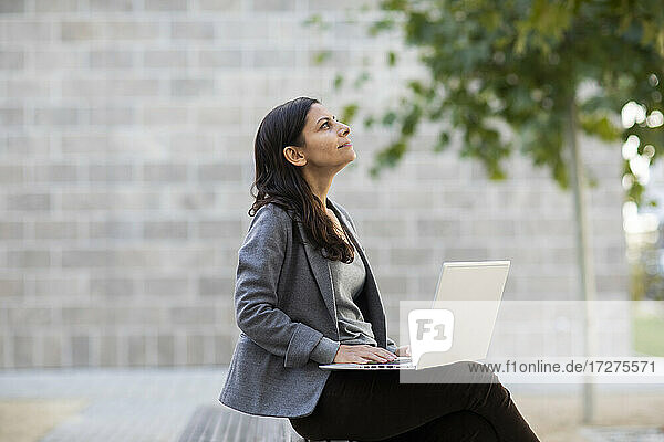 Geschäftsfrau  die einen Laptop benutzt und auf einer Bank an der Wand sitzt