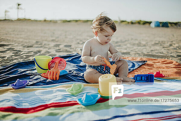 Kleiner Junge spielt mit Spielzeug am Strand bei Sonnenuntergang