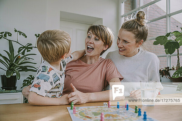 Fröhliche Mütter schauen zu  während ihr Sohn zu Hause ein Brettspiel spielt
