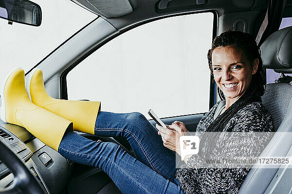 Lächelnde Frau mit Smartphone im Auto sitzend
