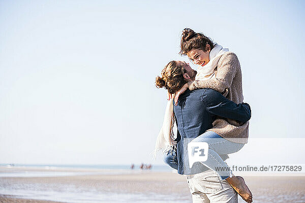 Glücklicher junger Mann mit Freundin am Strand gegen den klaren Himmel an einem sonnigen Tag