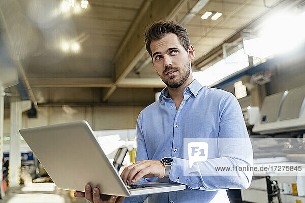 Businessman working on laptop while standing at factory