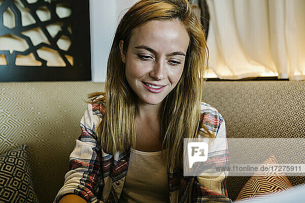 Lächelnde Geschäftsfrau mit Blick auf den Laptop  während sie zu Hause auf dem Sofa sitzt