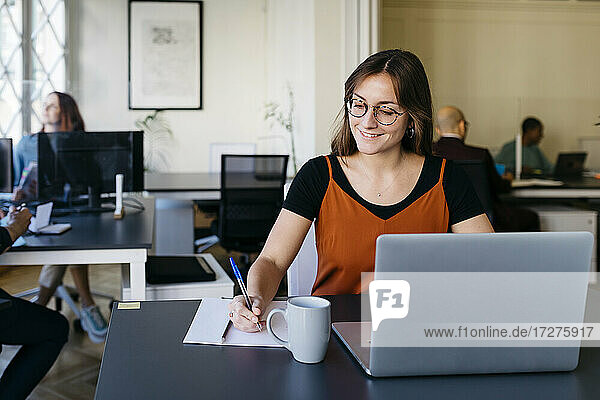 Smiling businesswoman writing while working at office desk