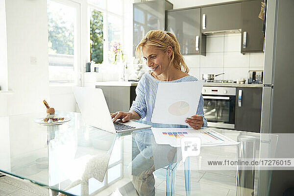Reife Frau arbeitet am Laptop  während sie in der Küche zu Hause sitzt