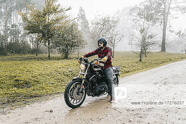 Man with motorcycle on dirt road in foggy weather