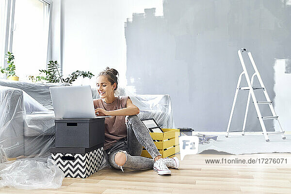 Lächelnde Frau arbeitet am Laptop  während sie zu Hause auf dem Sofa sitzt