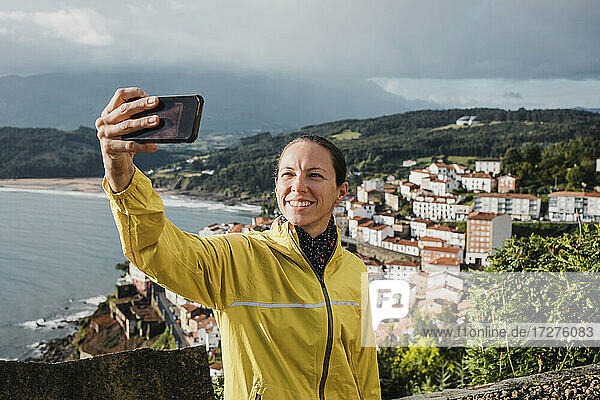 Lächelnde Frau  die in den Ferien ein Selfie mit ihrem Dorf per Handy macht