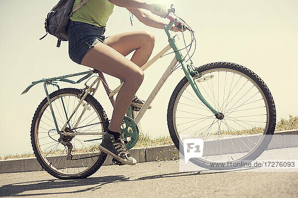 Legs of young woman riding bicycle on sunny day