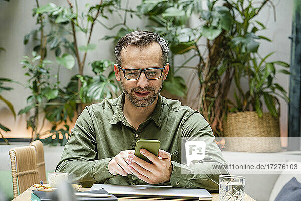 Smiling businessman using mobile phone while sitting at cafe