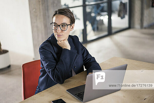 Businesswoman with head in hands looking away while working on laptop at office