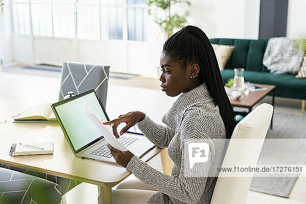 Eine Studentin liest eine Zeitung  während sie zu Hause am Laptop lernt