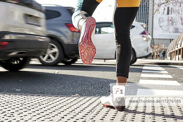 Young woman wearing sports shoe crossing road in traffic while running in city