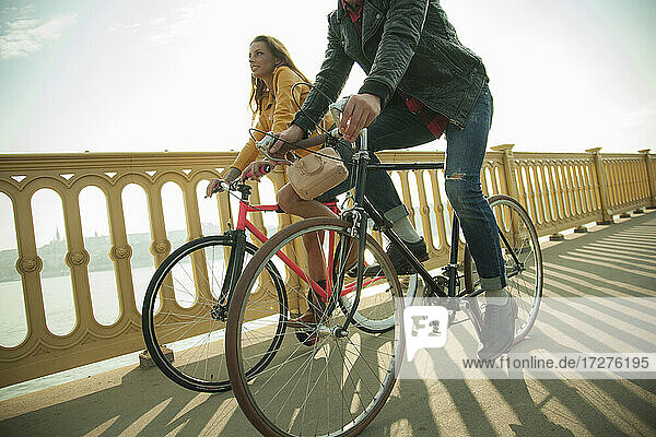 Heterosexuelles Paar fährt Fahrrad auf einer Brücke gegen den Himmel