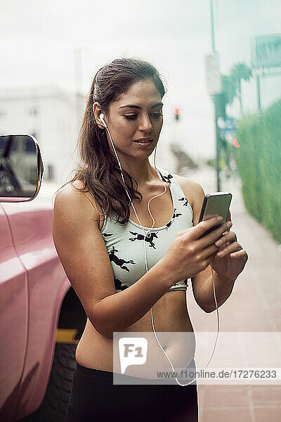 Young woman listening music through earphones while standing on street