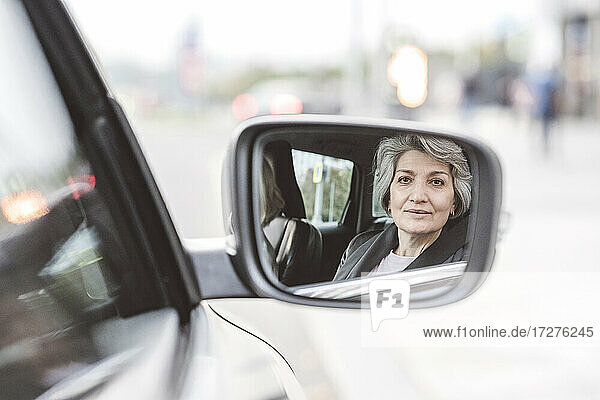 Spiegelung einer im Auto sitzenden Geschäftsfrau im Seitenspiegel
