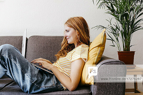 Redhead woman lying on sofa using laptop at home