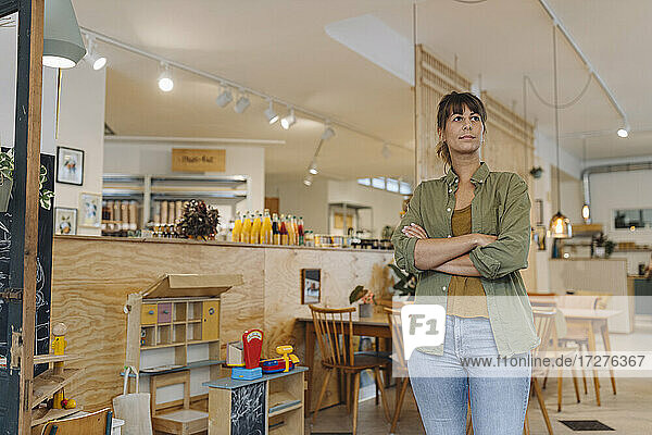Female owner with arms crossed looking while standing in cafe