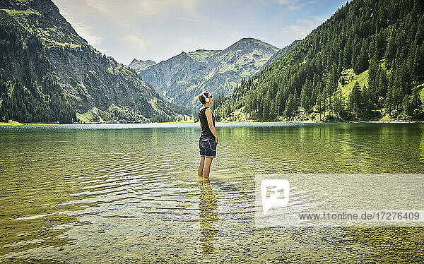 Mature woman standing knee deep in Vilsalpsee while listening music on sunny day