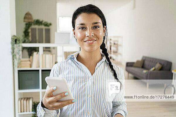 Lächelnde junge Frau  die ein Smartphone benutzt  während sie zu Hause steht