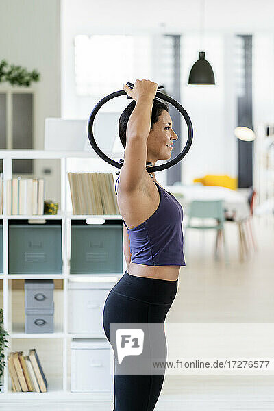 Young female exercising with pilates ring while standing at home